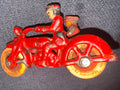A vintage red cast iron roller skate with yellow-orange wheels, photographed on a dark gray textured fabric surface.
