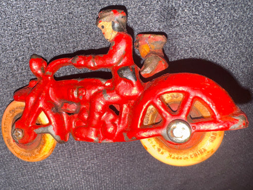 A vintage red cast iron roller skate with yellow-orange wheels, photographed on a dark gray textured fabric surface.